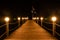 Illuminated wooden pier at night, lights on a wood bridge by the sea in Turkey. Seaside boardwalk with lanterns, round lamps.