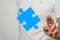 Illustration of a blue piece of a jigsaw puzzle next to a person\'s fingers