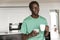 Image of african american man holding coffee cup and smartphone at home