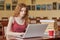 Image of attentive thoughtful young girl working on her laptop in library, putting away eyeglasses and cup of drink, searching for