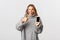 Image of attractive blond girl in grey sweater, looking satisfied and showing something good on smartphone screen, make