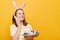 Image of attractive glad woman wearing rabbit ears holding Easter eggs and talking via mobile phone isolated on yellow background