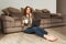 Image of attractive slim woman sitting on floor at home in living room, and working on notebook while drinking cup of tea