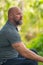 Image of a bald man with beard sitting outside and looking away from camera