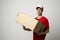 Image of bearded curly delivery man in red uniform with a blank cardboard, percel on white background.