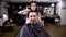 Image of bearded guy in barbershop covered with black peignoir.Female barber in casual clothes making stylish haircut