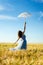 Image of beautiful blond young woman wearing long blue ball dress and holding white lace umbrella leaning up on wheat field