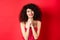 Image of beautiful curly-haired woman in red dress and makeup, saying thank you, looking grateful and smiling happy at