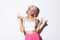 Image of beautiful girl in pink wig blowing chewing gum, popping bubble on face and showing peace signs, standing silly