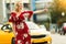 Image of blonde in red dress stopping taxi on summer.