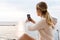 Image of blonde woman taking photo on cellphone while sitting on pier near seaside in morning