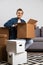 Image of brunet sitting on floor with cardboard boxes on background of gray sofa