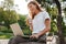 Image of caucasian modern woman sitting on bench in green park o