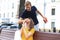 Image of charming excited couple in summer clothes smiling and holding present box together while sitting on bench