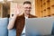 Image of cheerful adult man waving hand and working with laptop while