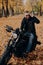 Image of cheerful male motorcyclist smiles joyfully, keeps hand on shades, sits on fast bike, has fun outdoor, enjoys traveling by