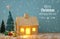 Image of christmas tree and wooden house with light through the window, over snowy table.