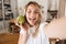 Image closeup of charming blond woman laughing and holding green apple while taking selfie photo in living room