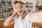 Image closeup of joyful blond woman laughing while taking selfie photo in living room