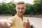 Image closeup of smiling middle-aged man taking selfie photo with thumb up while walking in summer park