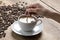 Image of a coffee cup being stirred by a white human hand, on a wooden table top