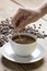 Image of a coffee cup being stirred by a white human hand, on a wooden table top