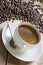 Image of a coffee cup and saucer with an old vintage spoon on a wooden table top. surrounded by raw coffee beans, taken at an