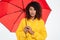 Image of confused african woman in raincoat hiding under umbrella