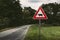 Image - Cow traffic european sign red triangle with curved road, green meadow and field on background on sunset. Beware of the