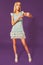 Image of cute beautiful slim blonde woman in elegant cocktail blue dress is posing at studio on purple background.