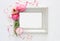 Image of delicate pastel pink beautiful flowers arrangement and empty vintage photo frame over white wooden background. Flat lay,