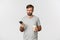 Image of disappointed frowning guy in gray t-shirt, drinking takeaway coffee and holding mobile phone, standing over