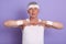 Image of energetic good looking pensioner stretching, standing isolated over lilac background in studio, looking directly at