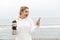 Image of excited blonde woman using earpods and cellphone while drinking water from bottle in boardwalk