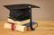 Image of graduation black hat over old books next to graduation on wooden desk. Education and back to school concept.