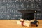 Image of graduation black hat over old books next to graduation on wooden desk. Education and back to school concept.