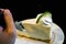 Image of hand holding a teaspoon is dividing a cake from a lime cream cake on a white ceramic plate