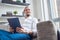 Image of happy brunet looking to side with tablet in his hands sitting on sofa in room.