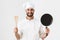Image of happy chief man in cook uniform holding wooden kitchen spatula and frying pan