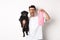 Image of happy man, pet owner, holding cute black pug and dog poop bag, standing over white background