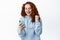 Image of happy and satisfied redhead woman rejoicing as looking at smartphone screen, achieve app goal, reading good