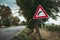 Image - Illuminated European traffic sign red triangle -curved road, green meadow and field on background on sunset. Beware of
