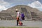 Image of an indigenous handicraft seller passing in front of one of the Teotihuacan pyramids