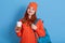 Image of joyful caucasian girl in hat drinking coffee while holding back pack, looks at camera, ginger lady has break between