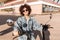 Image of joyful curly woman in sunglasses sitting on motorbike