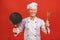 Image of joyful senior chief man in cook uniform smiling and holding frying pan isolated over red wall background