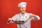 Image of joyful senior chief man in cook uniform smiling and holding frying pan isolated over red wall background