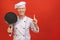 Image of joyful senior chief man in cook uniform smiling and holding frying pan isolated over red wall background