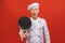 Image of joyful senior chief man in cook uniform smiling and holding frying pan isolated over red wall background