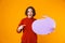 Image of joyous girl holding thought bubble with copyspace while standing isolated over yellow background